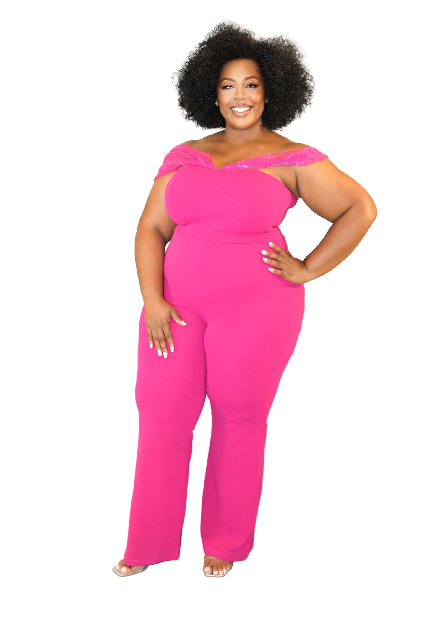 Woman wearing a bright pink jumpsuit with sheer shoulder details on a plain background