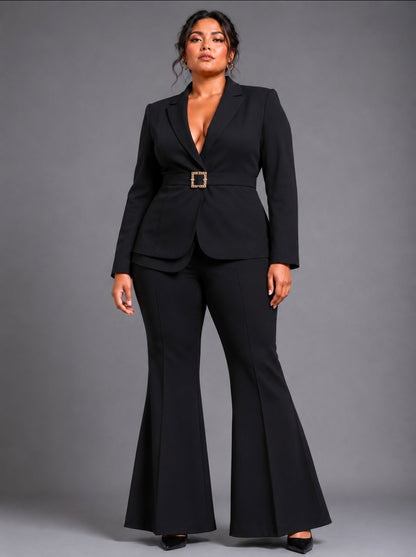 A woman modeling a black two-piece suit with a belted waist and flared pants, standing against a solid gray studio background.