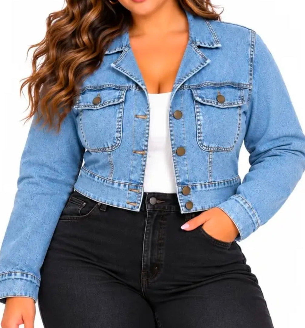 A woman wearing a cropped light blue denim jacket over a white top and black jeans, shown from the chin down against a plain white background.