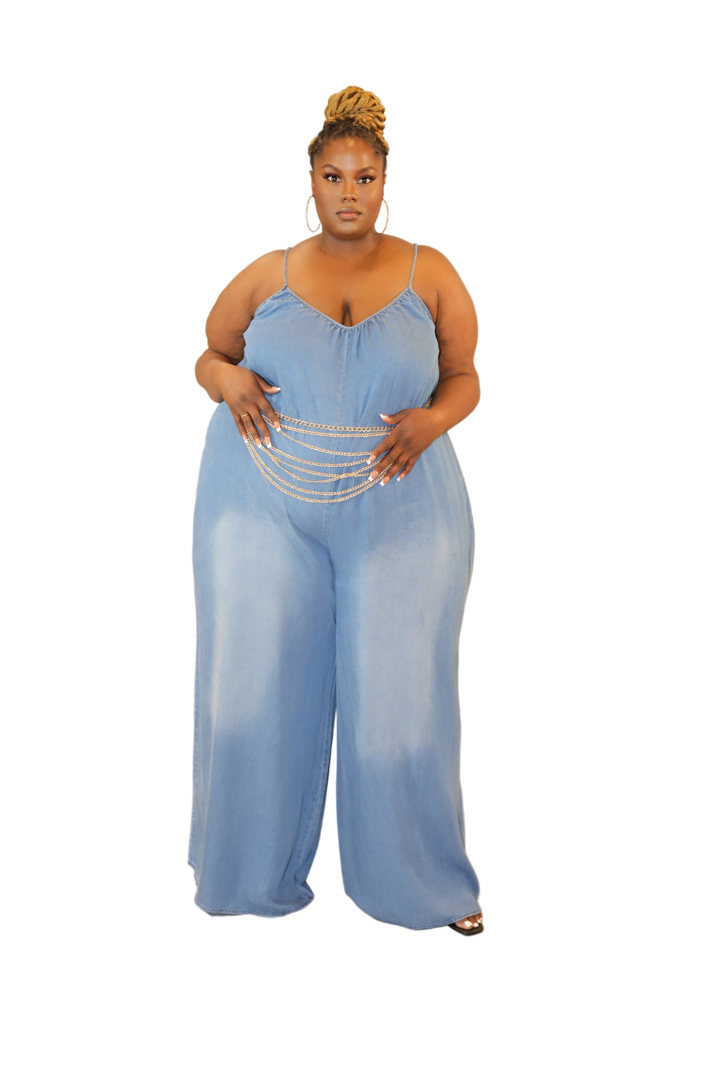 Woman wearing a light blue jumpsuit holding a gold clutch against a plain background