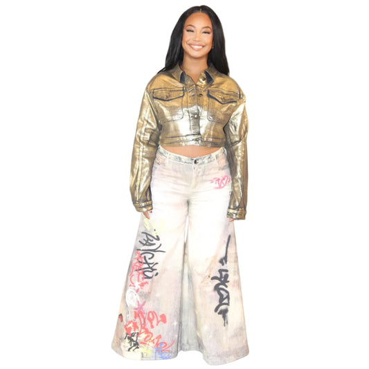 Woman wearing a gold jacket and light colored jeans on a white background. The jeans are detailed with multicolored graffiti. (front)