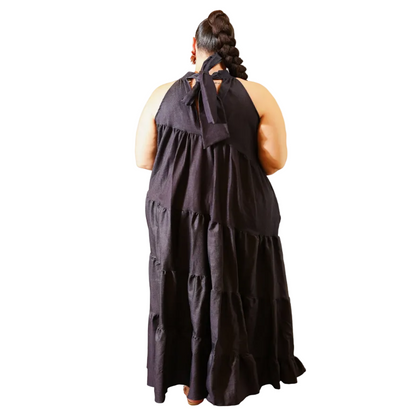 Woman wearing a dark denim halter neck dress with ruffled layers on a white background. (back)