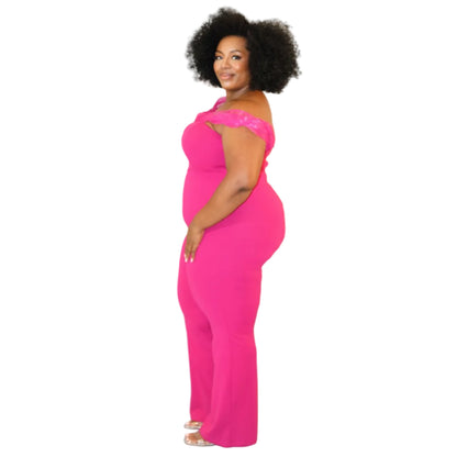 Woman wearing a bright pink jumpsuit with sheer off-the-shoulder sleeves on a white background. (left side)