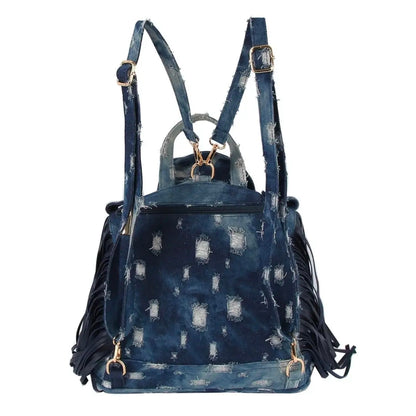 Dark blue denim bag with backpack straps, a handle, fringe, and gold hardware on a white background. (back)