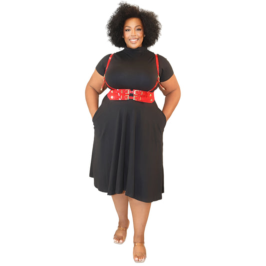 Woman wearing a black dress with a turtle neck and short sleeves, and a red harness with gold accents on a white background
