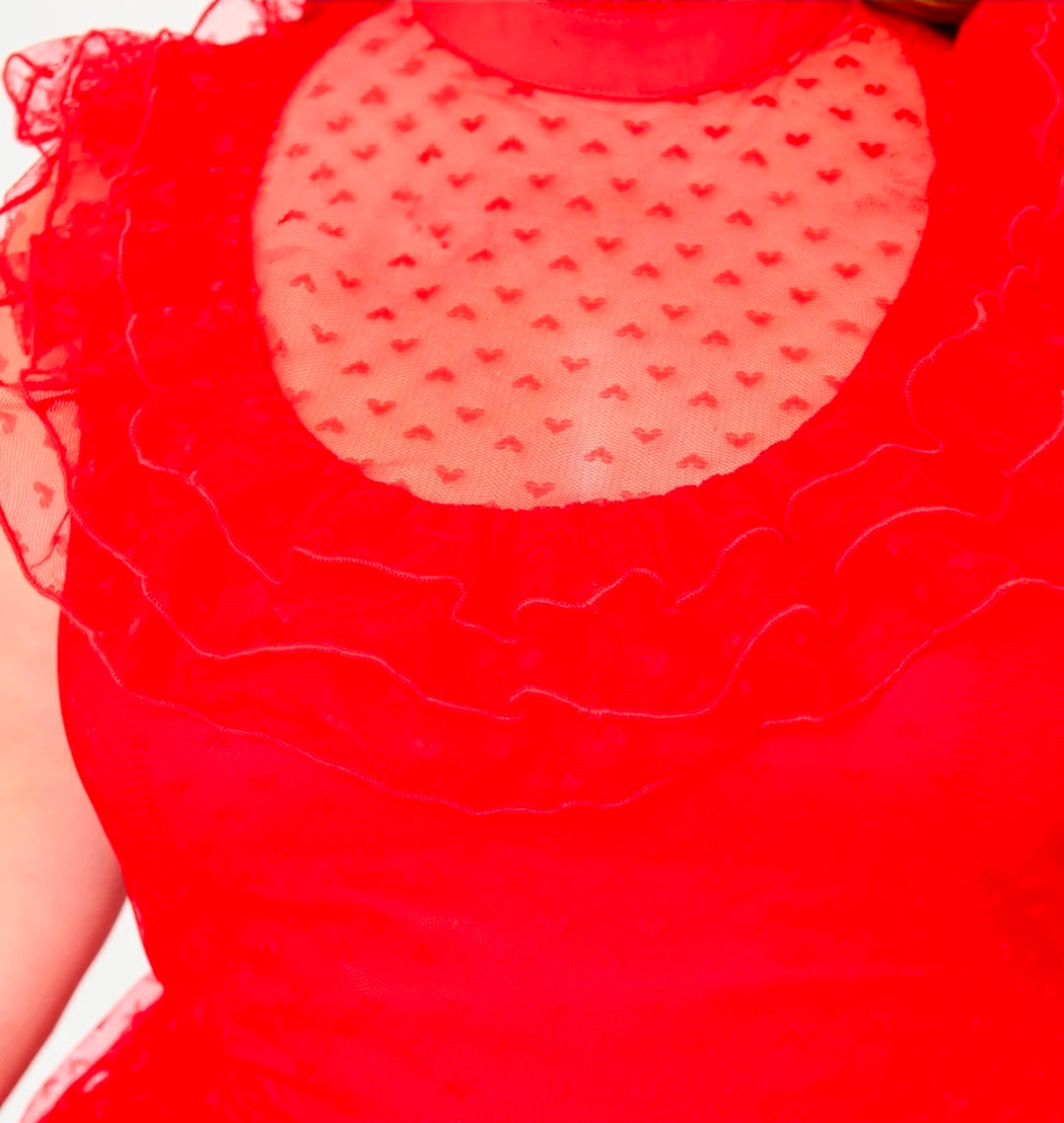 Close-up of a bright red sleeveless dress featuring a sheer heart-patterned mesh yoke and layered ruffled trim.
