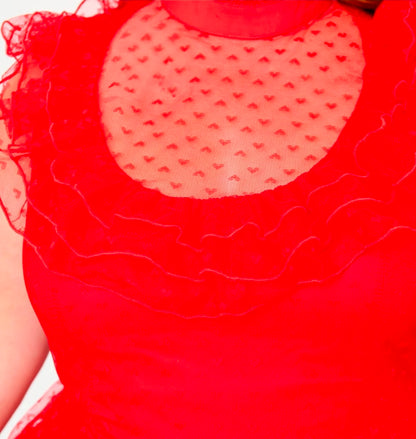 Close-up of a bright red sleeveless dress featuring a sheer heart-patterned mesh yoke and layered ruffled trim.