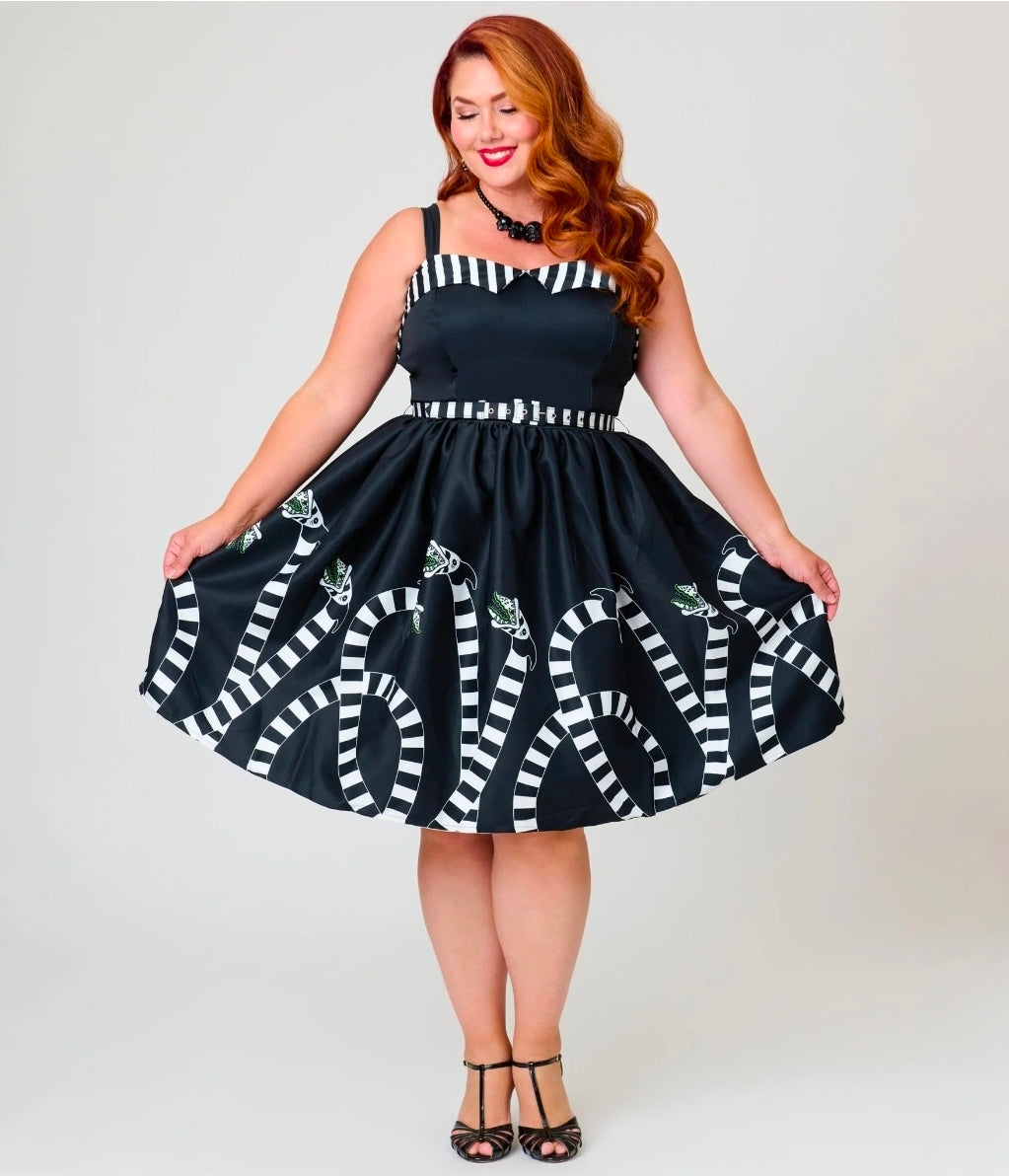 A woman modeling a black and white striped spaghetti-strap dress with a flared skirt, standing against a light gray studio background.
