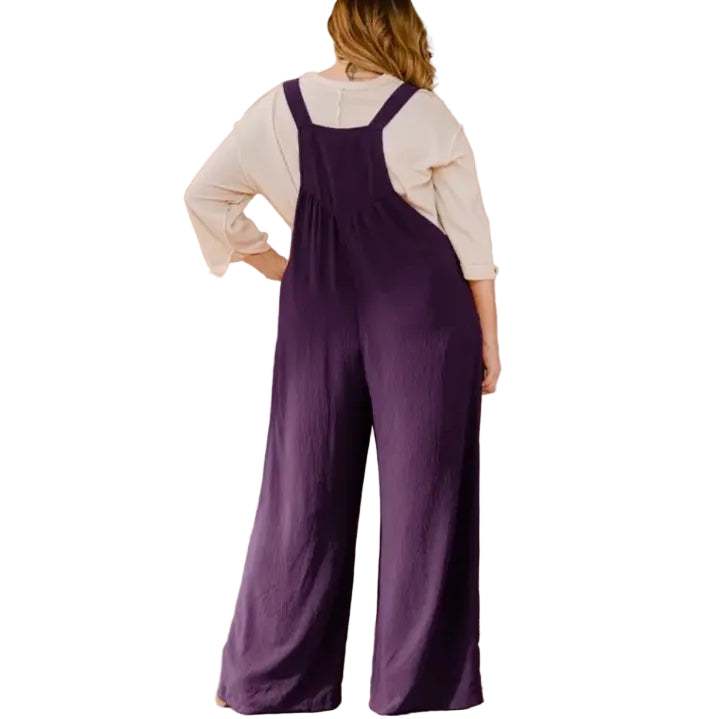 Woman wearing a white shirt and dark purple overalls on a white background.