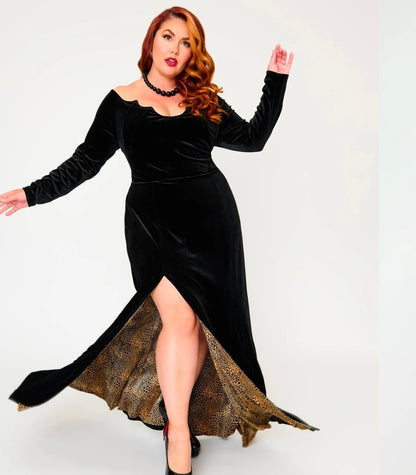 A woman modeling a long black velvet off-the-shoulder dress with a high slit and a gold patterned lining, posed against a light gray studio background.