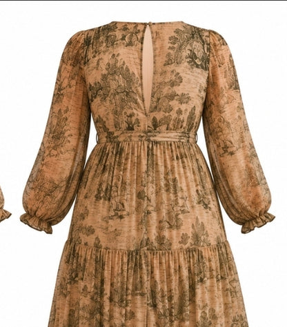 A long-sleeved midi dress with a tiered skirt and a deep V-back, featuring a brown and beige toile de Jouy floral pattern, shown against a plain white background.
