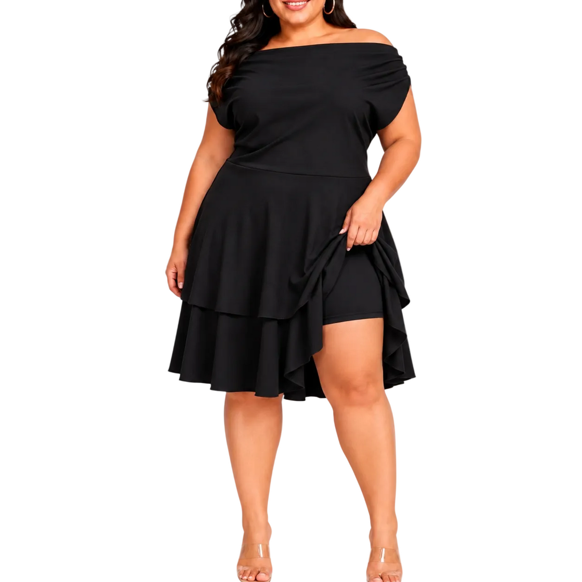 A woman modeling a black off-the-shoulder  dress with a layered ruffle skirt and attached shorts, paired with clear high-heeled sandals, against a white studio background